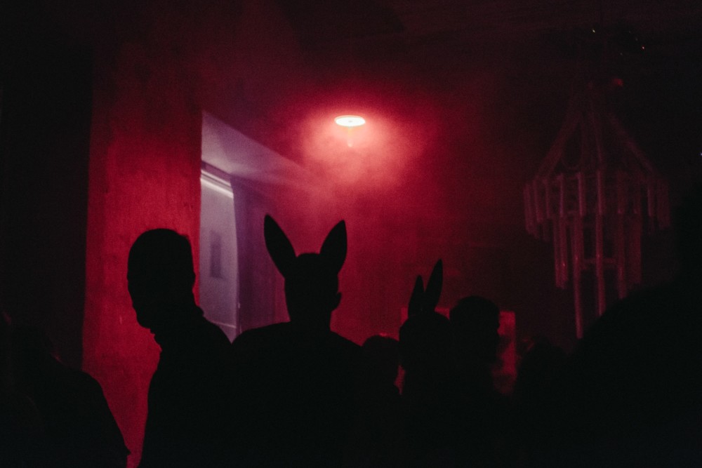 unkenntliche Menschen, eine Person mit Hasenohren, in einem dunklem Club unter rotem Licht