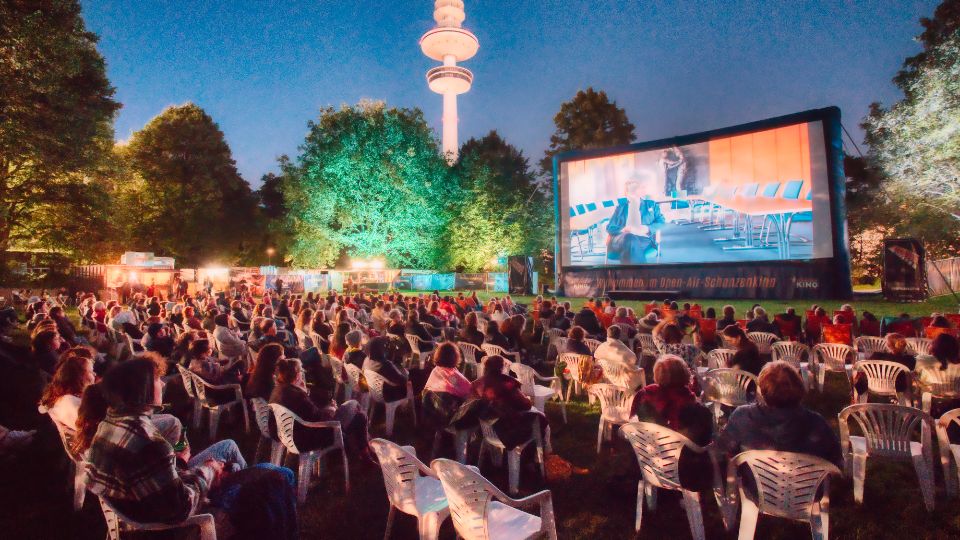 Bestuhltes Publikum vor einer Kinoleinwand im Schanzenpark in Hamburg. Im Hintergrund der Fernsehturm