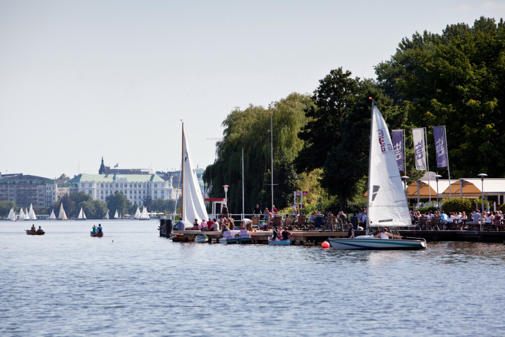 Ein Anleger auf der Außenalster, mit zwei Segelbooten und im Hintergrund die Stadt