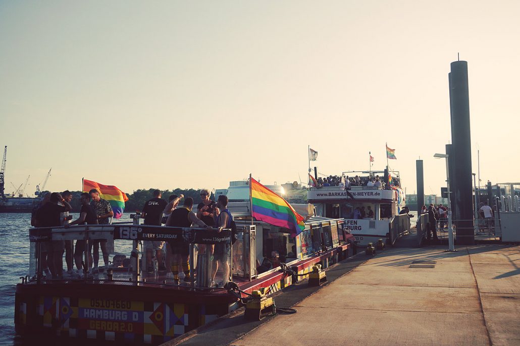 zwei Boote liegen am Anleger, auf ihnen wird zur Hamburg Pride Week gefeiert und Regenbogenflaggen wehen im Wind