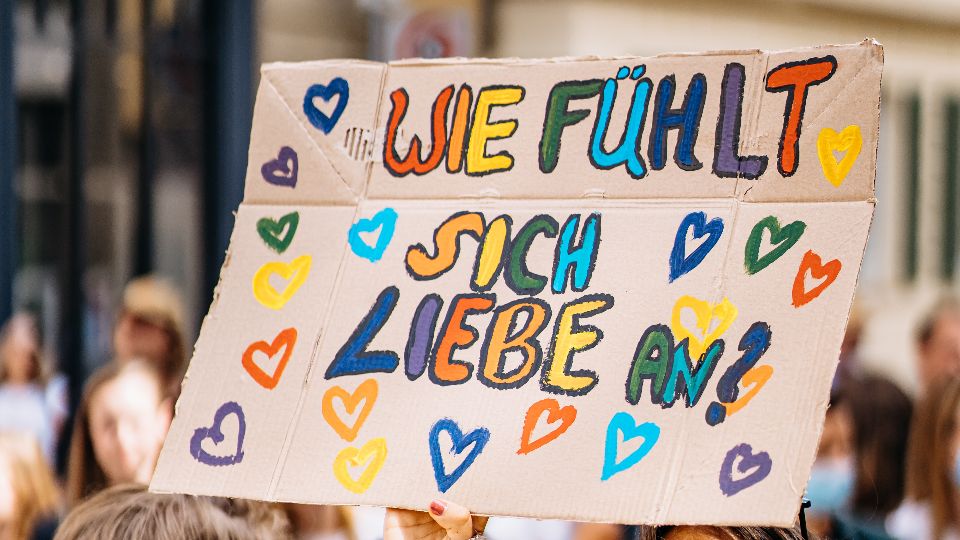 ein selbstgebasteltes Pappplakat mit der bunten Aufschrift "Wie fühlt sich Liebe an?"