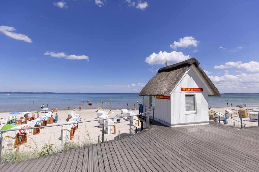 Ein kleines weißes DLRG-Häuschen mit Reetdach am Strand der Lübecker Bucht in Scharbeutz im Sommer