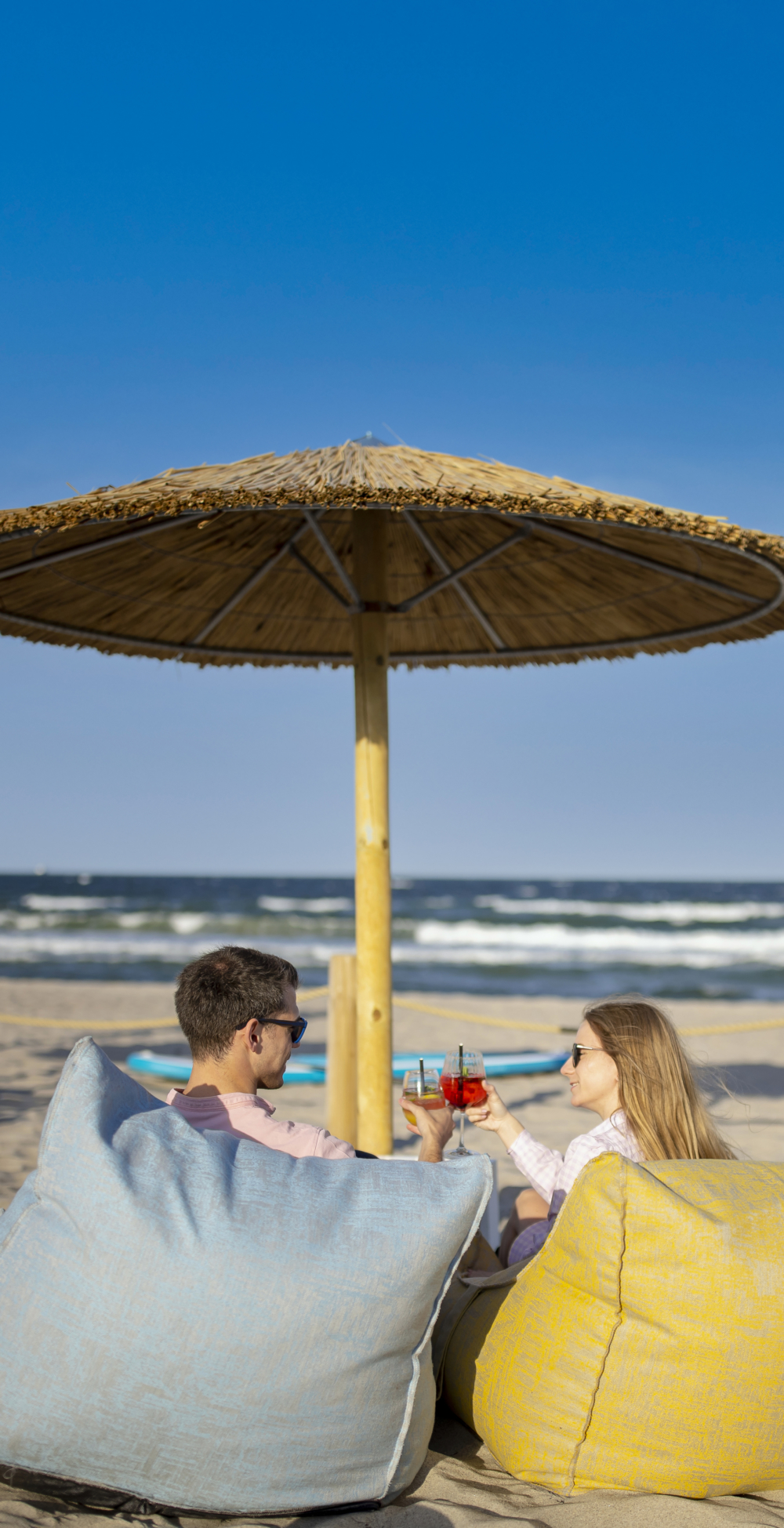 Ein Paar stößt mit Drinks bei Sonnenschein an. Sie sitzen in Sitzsäcken am Strand in Haffkrug an der Lübecker Bucht