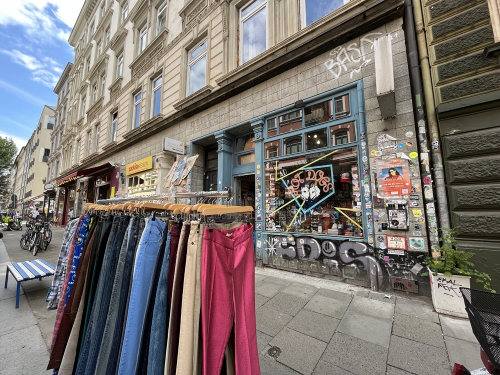 Außenansicht eines Vintage-Stores in Hamburg mit Graffiti und Plakaten und einem Kleiderständer mit Hosen vor dem Laden