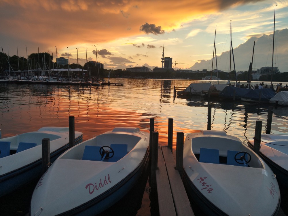 weiße Tretboote liegen im Sonnenuntergang an einem Bootsverleih auf der Alster in Hamburg