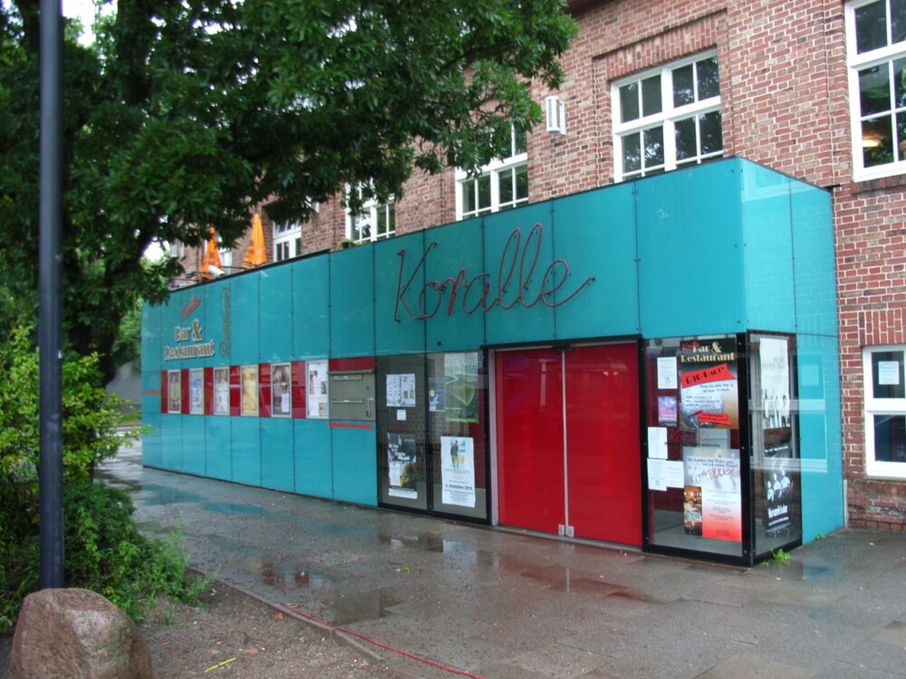 ein türkiser Vorbau mit Schriftzug und roter Eingangstür weist auf das Koralle Kino in Volksdorf hin