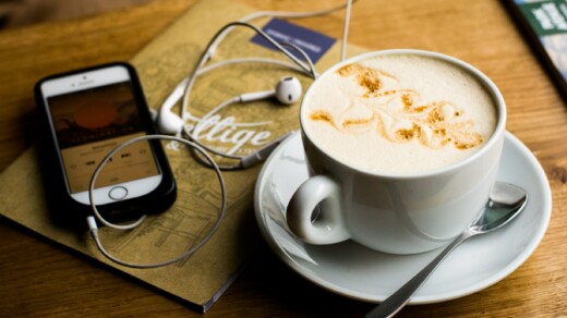 Tisch mit Cappuccino-Tasse daneben liegt ein Smartphone mit Kopfhörern
