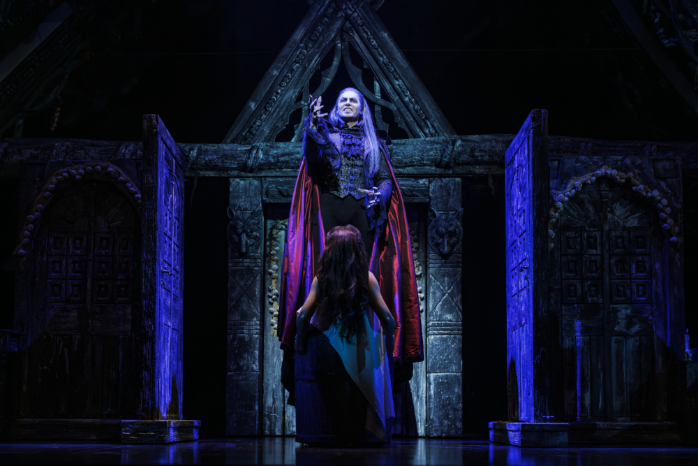 Szene aus dem Musical Tanz der Vampire: Vampir in roter Robe in mächtiger Pose vor einer ihm zugewandten Frau