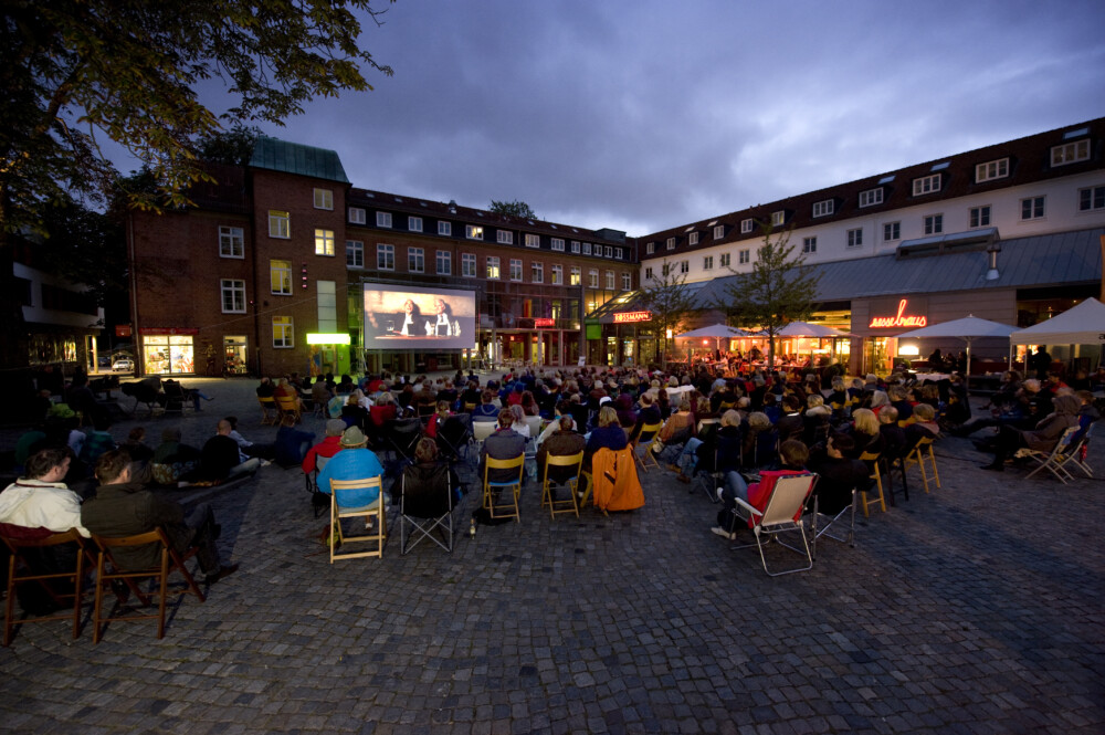 Das Foto zeigt: mehrere Menschen, die auf Klappstühlen vor der Leinwand des Sommerkinos sitzen.