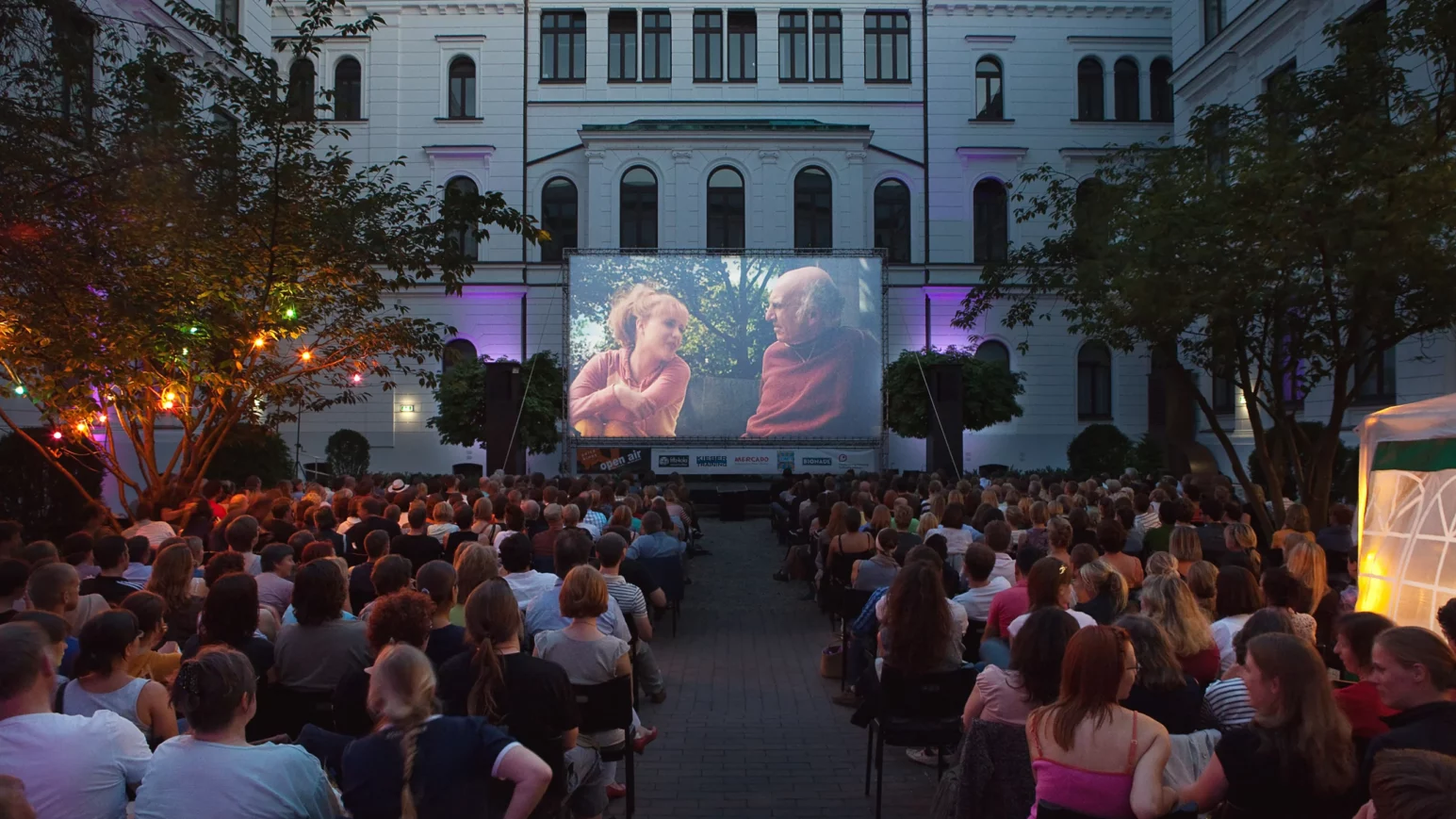 Draußen Kino mit Leinwand und Personen auf Stühlen davor