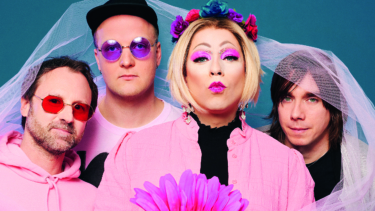 Vier pink gekleidete Personen mit einer großes ebenfalls pinken Blume in der Hand