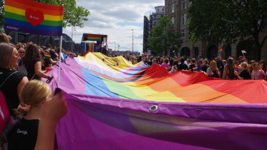 Menschenmenge, die eine große bunte Pride Flagge halten