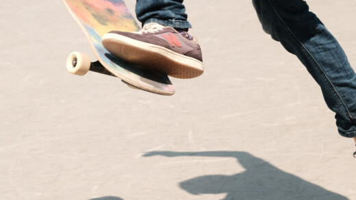 Longboarder springt mit buntem Board, sein Schatten fällt auf den Boden