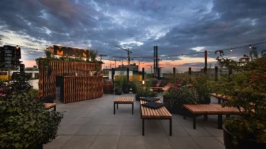 Dachterrasse mit Holzmöbeln und Pflanzen bei Sonnenuntergang unter bewölktem Himmel in einer Stadt