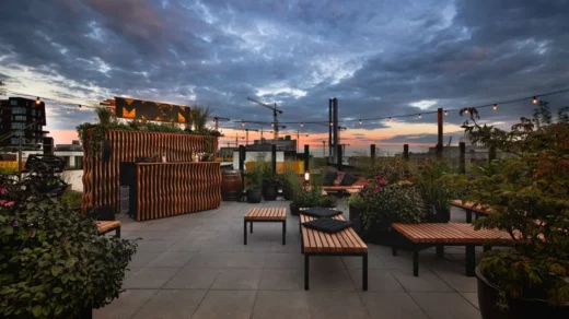 Dachterrasse mit Holzmöbeln und Pflanzen bei Sonnenuntergang unter bewölktem Himmel in einer Stadt