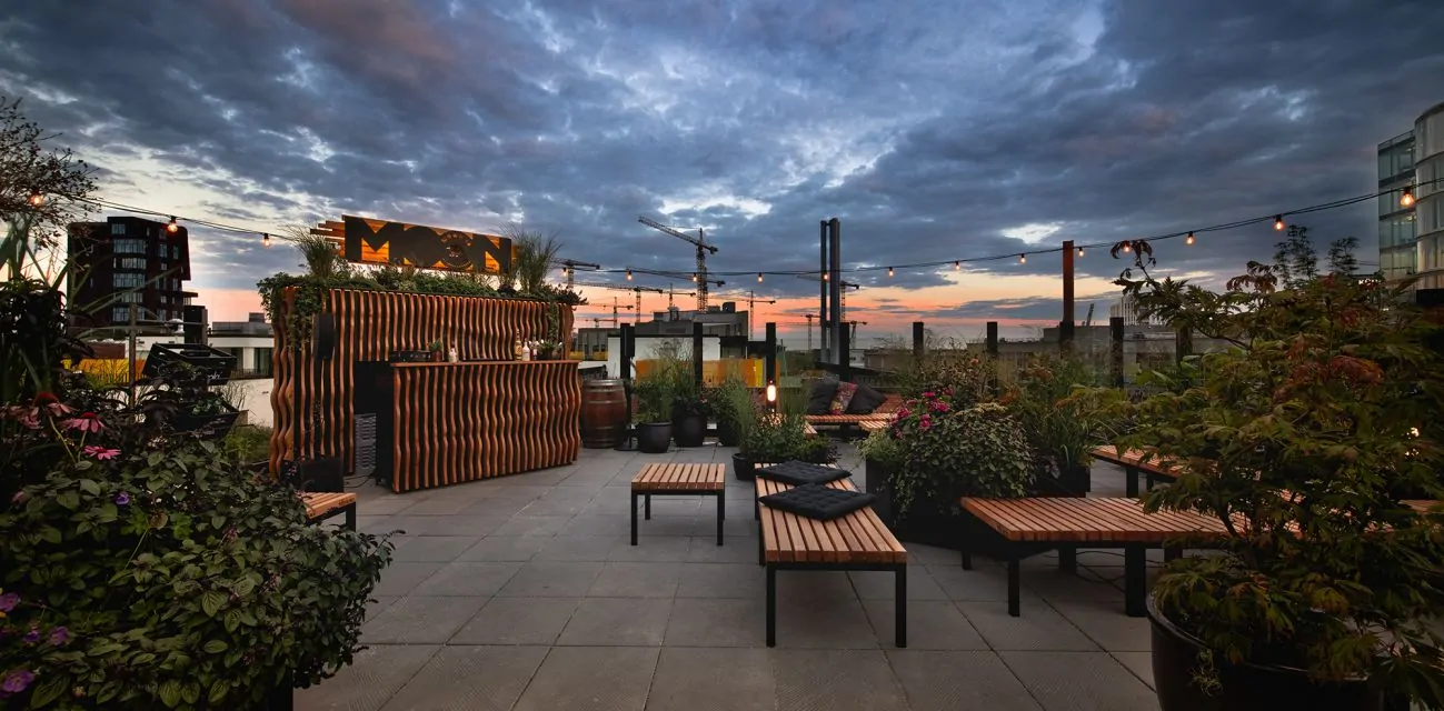 Dachterrasse mit Holzmöbeln und Pflanzen bei Sonnenuntergang unter bewölktem Himmel in einer Stadt