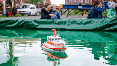 Eine Person mit einem Kind auf dem Arm -davor Wasser mit einem Plastik Boot
