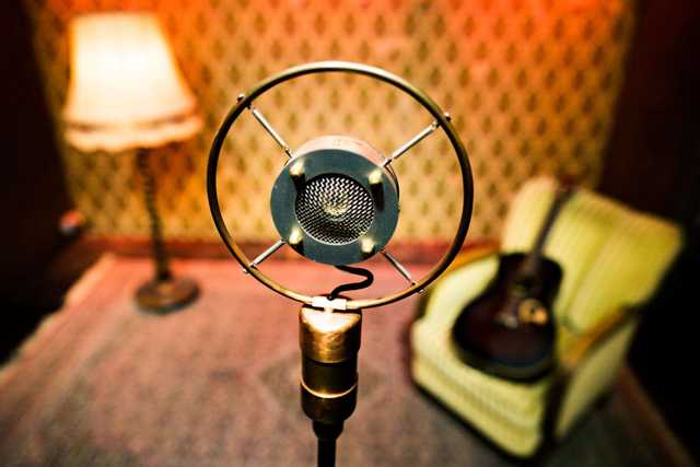 Nahaufnahme eines Vintage-Rundfunkmikrofons mit Ringhalterung vor einem Sessel mit Gitarre und einer Stehlampe