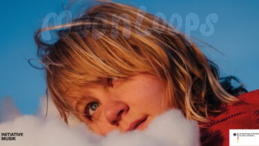 Person mit langen, blonden Haaren trägt rote Jacke vor blauem Himmel mit Wolken