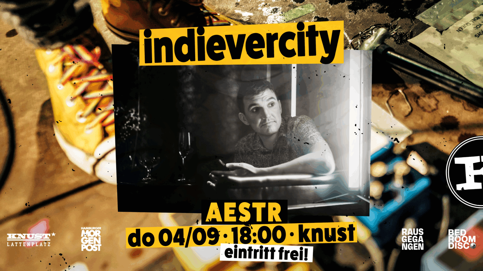 Person sitzt mit ausgestrecktem Arm an einem Tisch, umgeben von gelben Stiefeln und verstreuten Gegenständen, Text 'indieverity' und 'AESTR do 04/09 18:00 knust eintritt frei!'