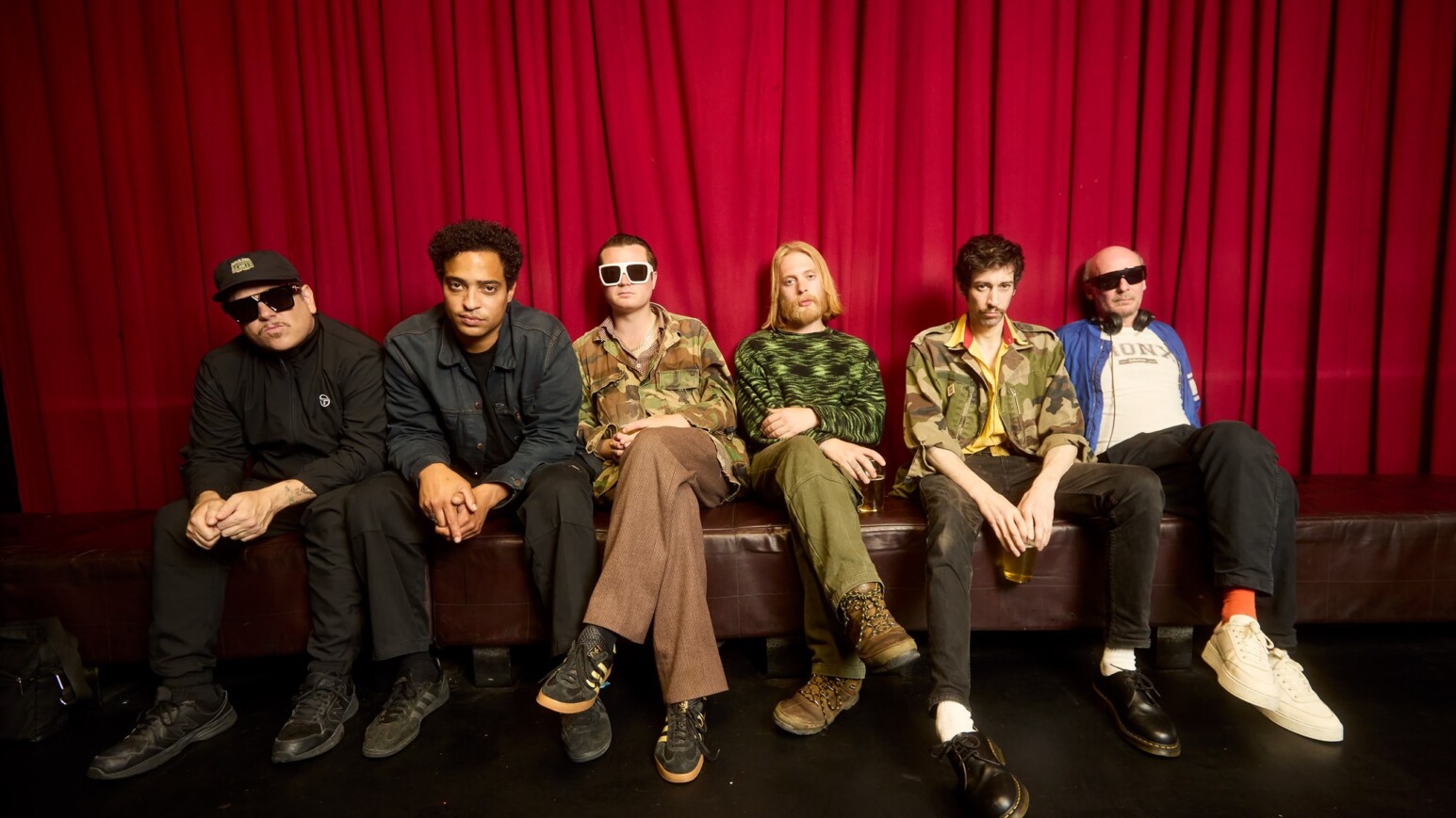 Ein Bild der Band "Warmduscher" auf einem Sofa vor einem roten Vorhang