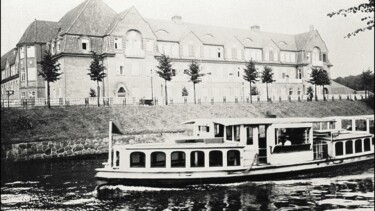 Ein schwarz-weiß Bild mit einem Schiff auf einem Fluss im Zentrum - Im Hintegrund das Gebäudes der U-Bahnstation Mundsburg