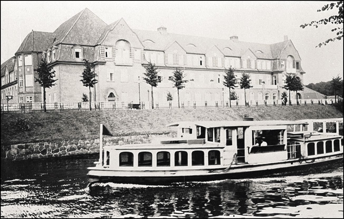 Ein schwarz-weiß Bild mit einem Schiff auf einem Fluss im Zentrum - Im Hintegrund das Gebäudes der U-Bahnstation Mundsburg
