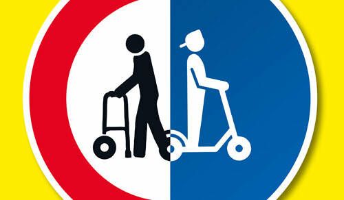 Ein Schild rund zweigeteilt vor gelbem Hintergrund - Eine Figur mit einem Rollator vor einem weißen Hintergrund mit roten Rand - Auf der anderen Seite eine Figur auf einem Roller vor blauem Hintergrund