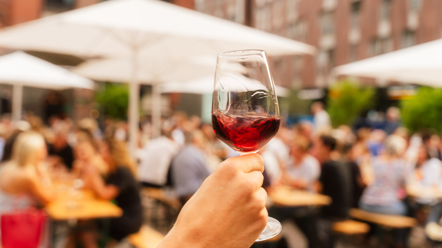 Vordergrund - Ein Wein der gehalten wird und im Hintergrund - Personen auf Bierbänken