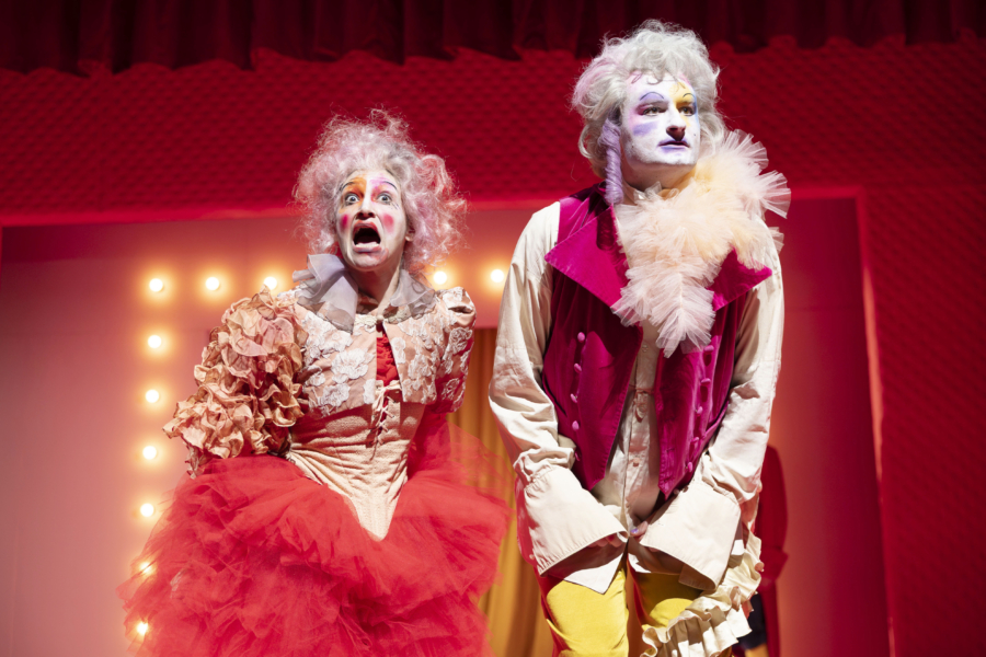 Zwei bunt gekleidete und geschminkte Theaterdarsteller:innen auf der Bühne.