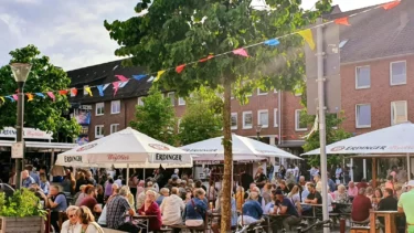 Großer Platz mit Menschen und Sitzgelegenheiten und Bierwagen vor einer Häuserreihe