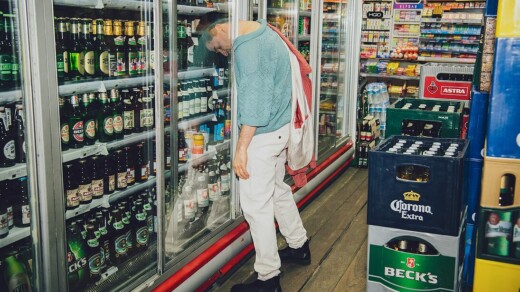 Eine Person in einem Kiosk die mit dem Kopf zwischen den Scheiben des Getränke-Kühlschranks steckt
