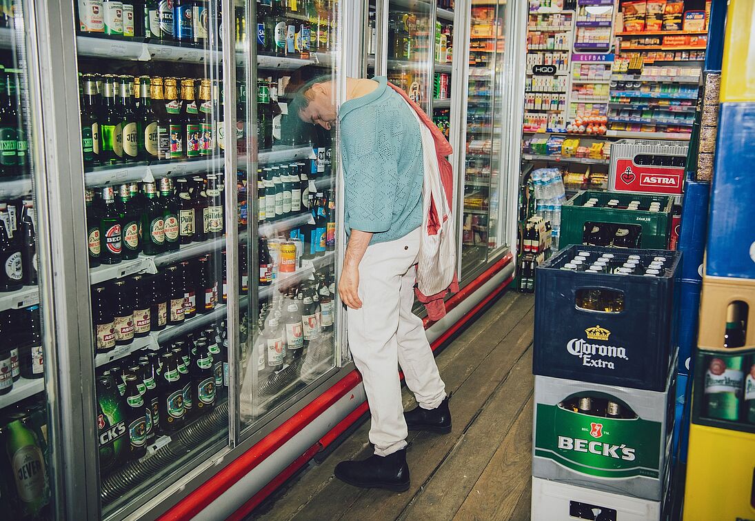 Eine Person in einem Kiosk die mit dem Kopf zwischen den Scheiben des Getränke-Kühlschranks steckt