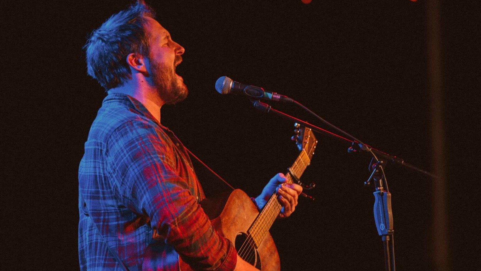 Person die mit einer Gitarre in ein Mikrofon singt