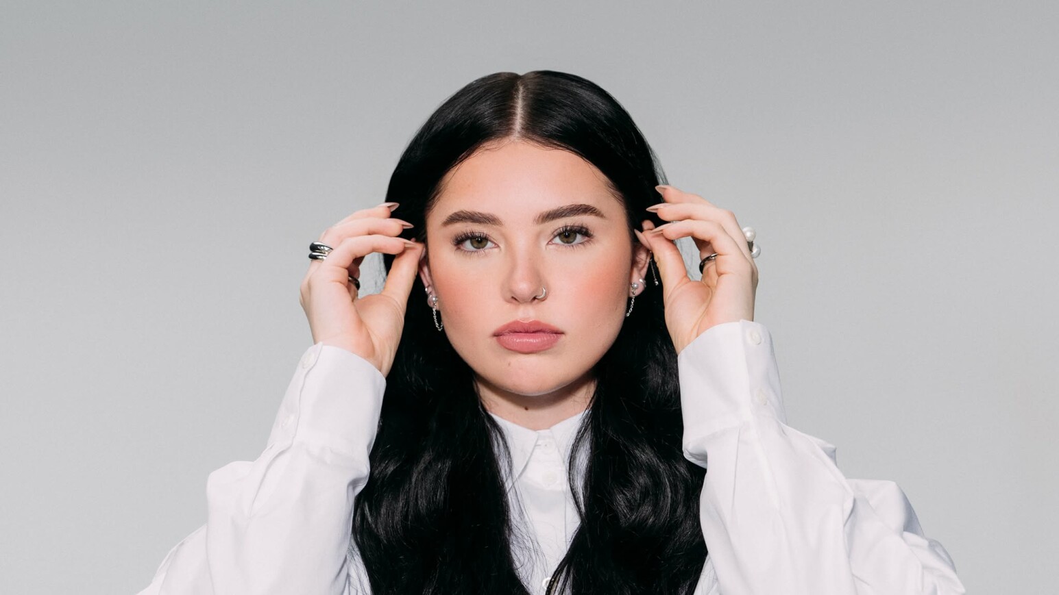 Lauren Spencer Smith trägt ein weißes Hemd und hält ihre Haare mit beiden Händen. Sie hat lange, schwarze Haare und trägt mehrere Ringe.