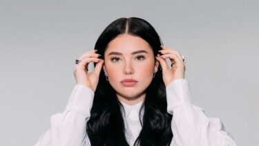 Lauren Spencer Smith trägt ein weißes Hemd und hält ihre Haare mit beiden Händen. Sie hat lange, schwarze Haare und trägt mehrere Ringe.