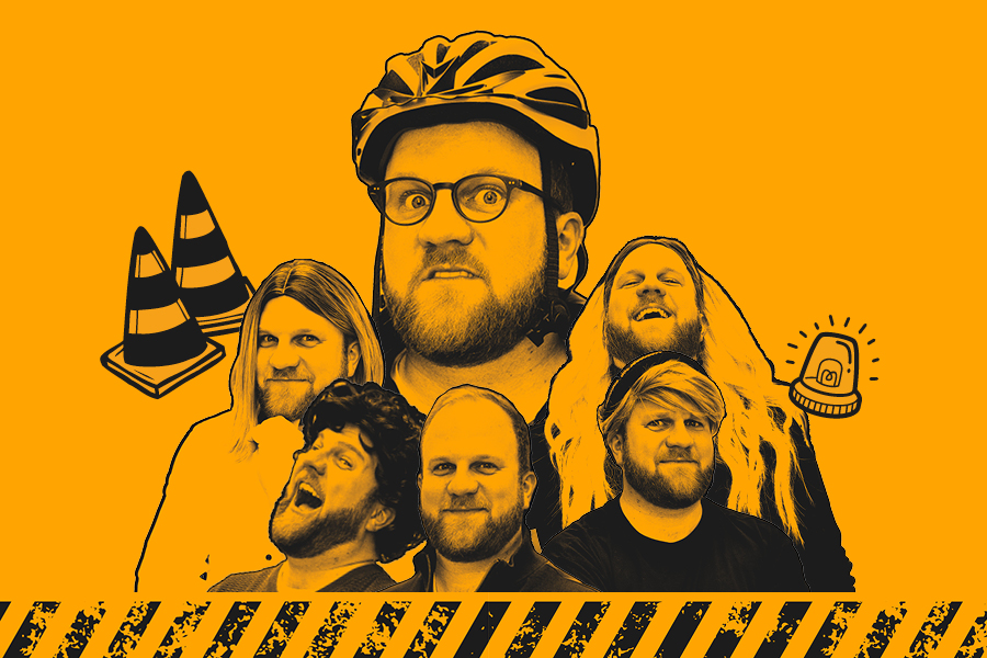 Fünf Personen vor orangefarbenem Hintergrund, eine trägt einen Fahrradhelm, zwei orange-weiße Verkehrskegel und ein blinkendes Warnlicht sind sichtbar.