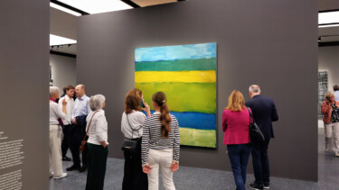 Besucher stehen vor einem großen abstrakten Gemälde mit horizontalen Streifen in Blau, Grün und Gelb in einer Galerie.