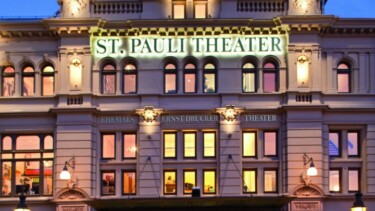 Das St. Pauli Theater mit einer hell erleuchteten Fassade, großen Fenstern und dem Schriftzug 'ST. PAULI THEATER' über dem Eingang.