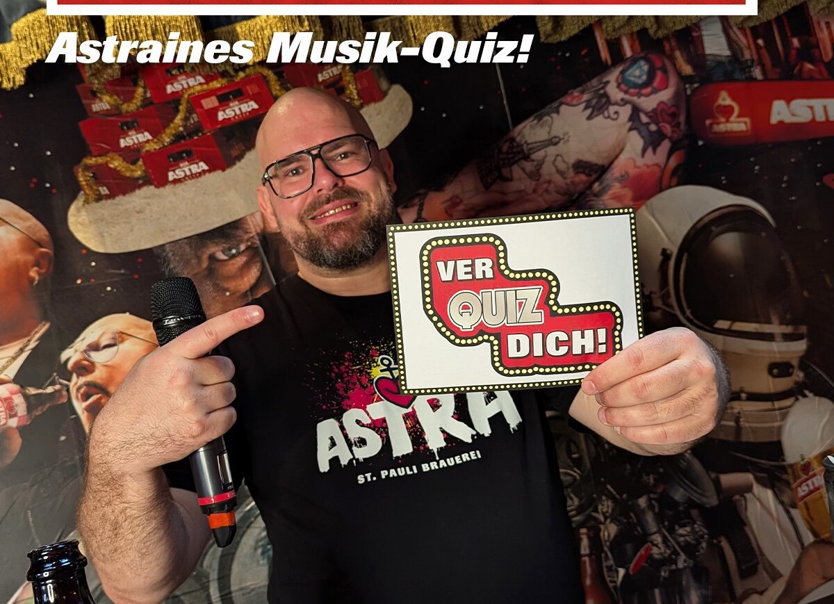 Person hält Mikrofon und Schild mit Aufschrift 'VER QUIZ DICH!' vor einem Hintergrund mit Astra-Logos und Weihnachtsdekoration.