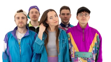 Fünf Personen in bunter Freizeitkleidung, darunter eine Frau mit langem Haar und grauem Oberteil, stehen nebeneinander.