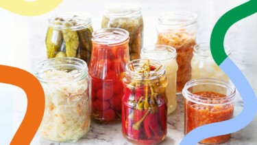 Verschiedene Einmachgläser mit eingelegtem Gemüse wie Gurken, Paprika und Sauerkraut auf Marmoroberfläche, umrahmt von bunten Linien.