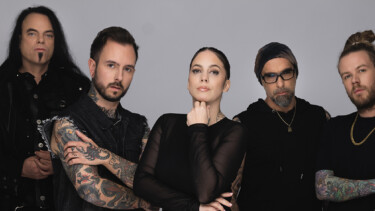 Fünf Personen in dunkler Kleidung, einige mit sichtbaren Tattoos an Armen, vor neutralem Hintergrund.