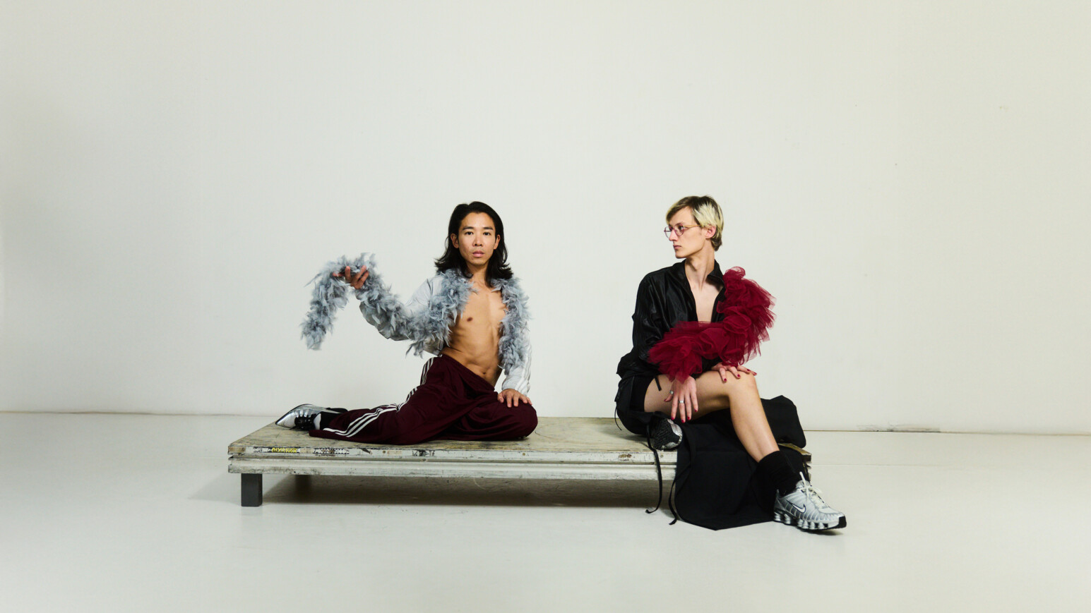 Die Hamburger Künstler:innen Lisa Rykena und Carolin Jüngst sitzen auf einer Bank vor einem weißen Hintergrund