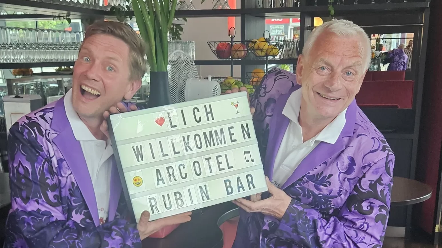 Zwei Männer im lilanen Anzug, die jeden in der Artecol Rubin Bar willkommen heißen