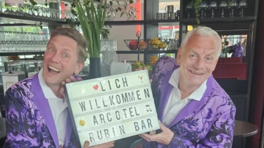 Zwei Männer im lilanen Anzug, die jeden in der Artecol Rubin Bar willkommen heißen
