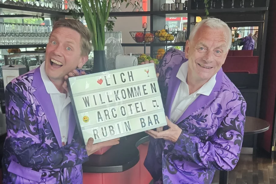 Zwei Männer im lilanen Anzug, die jeden in der Artecol Rubin Bar willkommen heißen