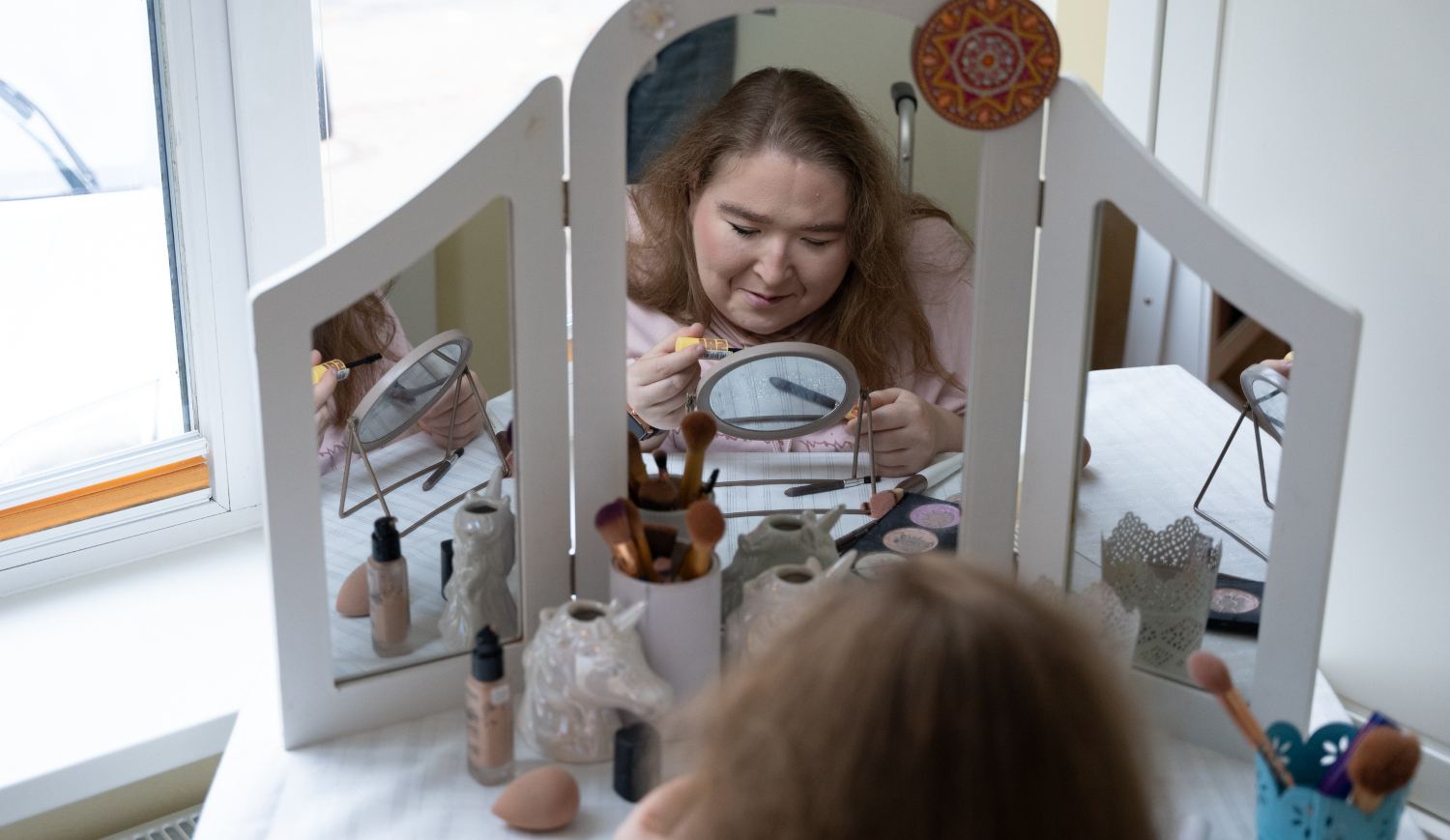 Eine Frau schminkt sich am Schminktisch vor dem Spiegel