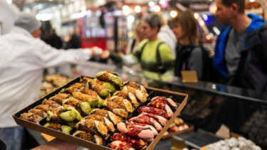Auf einer Messe hält eine nicht gezeigte Person einen Teller mit Cannoli hoch