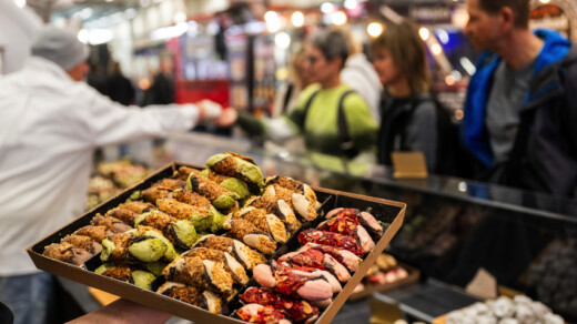 Auf einer Messe hält eine nicht gezeigte Person einen Teller mit Cannoli hoch